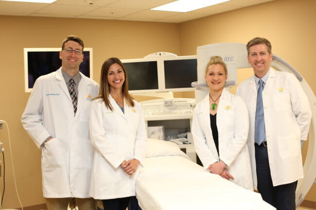 Twin Cities Pain Clinic Doctors posing around a hospital bed in procedure room